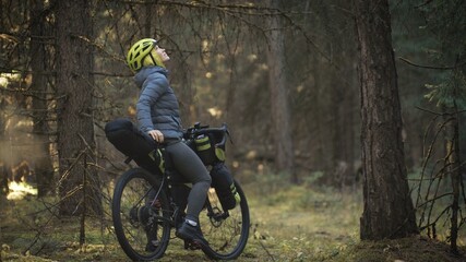 Obraz premium The woman travel on mixed terrain cycle touring with bike bikepacking outdoor. The traveler journey with bicycle bags. Stylish bikepacking, bike, sportswear in green black colors. Magic forest park.
