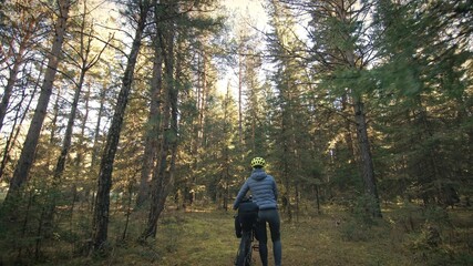 Fototapeta premium The woman travel on mixed terrain cycle touring with bike bikepacking outdoor. The traveler journey with bicycle bags. Stylish bikepacking, bike, sportswear in green black colors. Magic forest park.