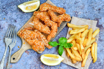 
 Crispy  deep fried   chicken strips  with sesame seeds and french fries . Breaded  with cornflakes chicken  breast fillets  with chilly peppers and fresh   basil on wooden rustic background
