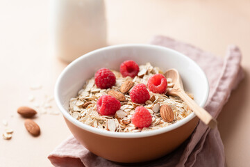 Oat muesli with raspberries and almonds in ceramic bowl served with almond milk. Healthy breakfast food