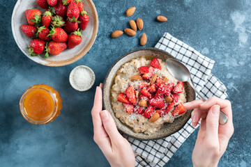 Female hands holding bowl of oatmeal with strawberries, almonds and honey. Eating healthy food. Top view