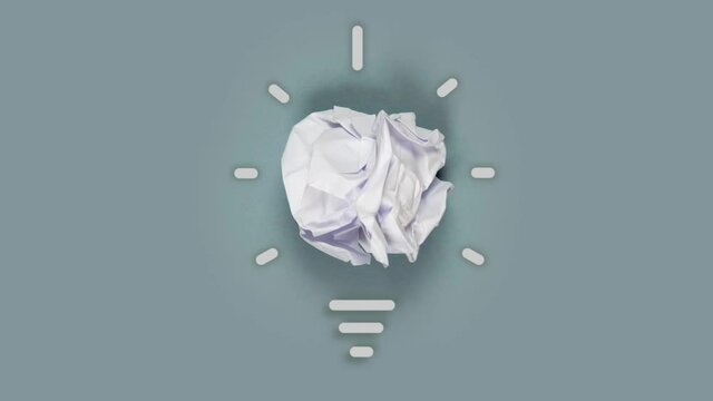 Paper being crumbled into a yellow light bulb on gray background. Concept of Innovation and Creativity . High quality 4k video.