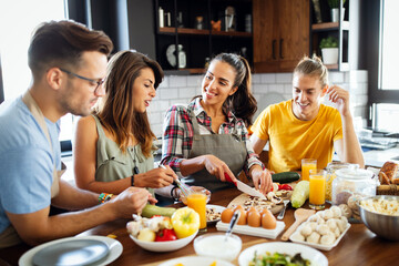 Group of happy friends laughing and talking while preparing meals in kitchen