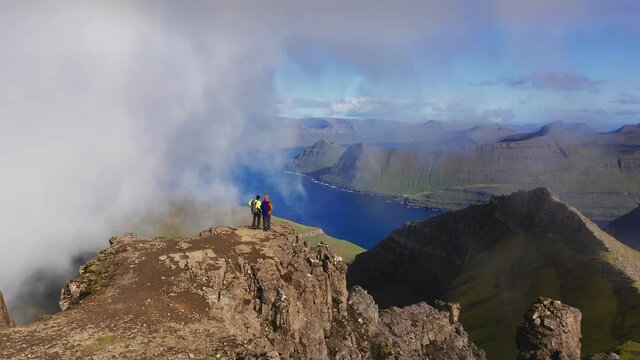 Aerial view of two people on the top of mountain looking the beautiful landscape, sea, cliff, mountain, rocky, wrapping by clouds