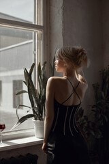 Naklejka premium Retro portrait sexy blonde woman in black dress, vintage interior woman posing at window. Sensual romantic look, girl relaxes at home