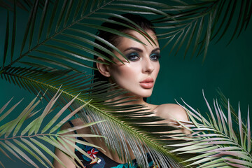 Tropical portrait sexy woman in leaves palm tree. Bright green makeup, shadow of palm leaves on...