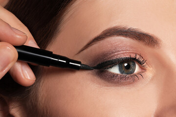 Artist applying black eyeliner onto woman's face, closeup