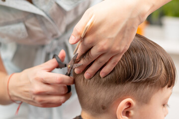 caring female hands of a mother with a comb and scissors make a fashionable haircut for her son at home during the second lockdown. selective focus