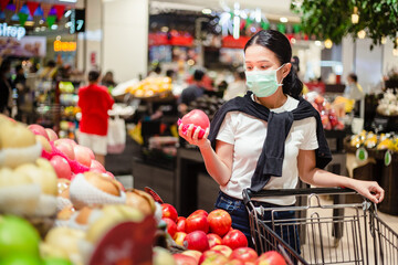 Young woman with face mask buying some fruit in supermarket during virus outbreak. Asian woman shopping during coronavirus crisis or covid19 outbreak.