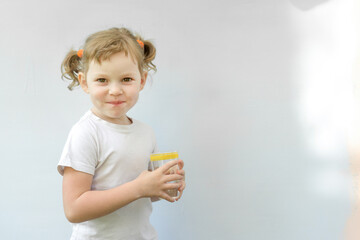 Little Caucasian child girl of five years old with a glass of water looking at the camera on a light sunny background. Curly blonde girl. Healthy lifestyle concept.