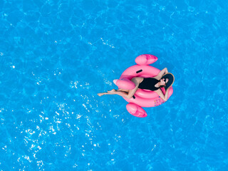Summer background. Beautiful woman floating on pool flamingo float in pool in hotel. Summer holidays, enjoying summer vacations during quarantine. Aerial drone view