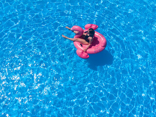 Beautiful woman on flamingo pool float in pool in the hotel, drone aerial view. Summer holidays