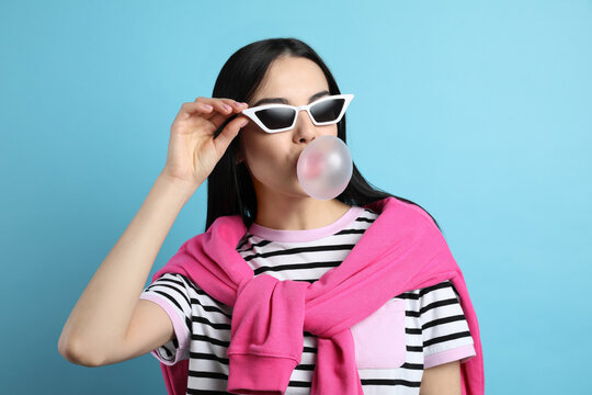 Fashionable young woman blowing bubblegum on light blue background
