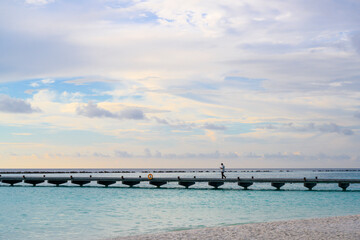 A man in a medical mask walks along a long pier that goes out to sea