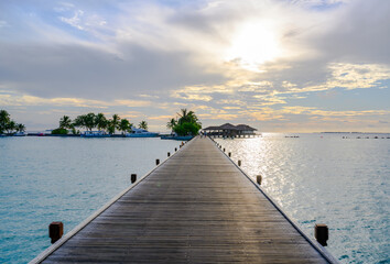 Fototapeta premium Boats, palm trees and a wooden pier stretching out into the ocean under the evening cloudy sky