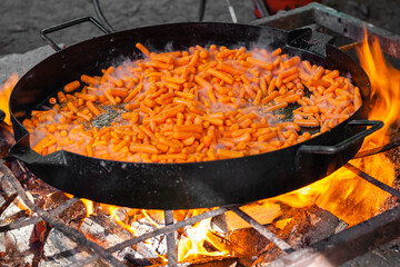 Huge pan of grilled carrot cooking for catering, horizontal close-up shot of fire-fried food with wooden spoon for the restaurant on the street. 