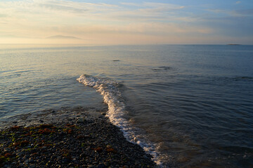 The sunrise over the calm sea casts rays of orange light into the air as the setting sun penetrates through the clouds into the picturesque calm seascape, the sea.