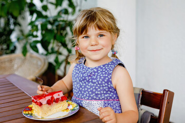 Little preschool girl with strawberry cake. Happy child eating cake with fresh strawberries. Summer dessert for families.
