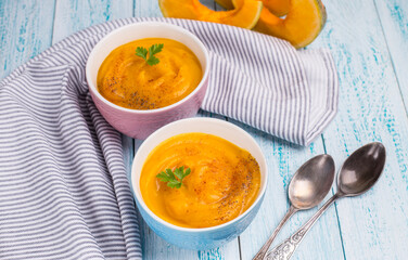 Traditional autumn pumpkin soup with bright masks on a blue background. Vegetarian delicious food.