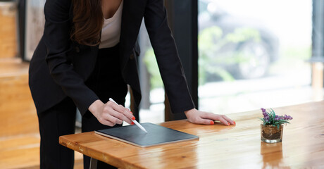 Close up view of business woman holding stylus pen and using digital tablet on wooden desk at cafe.