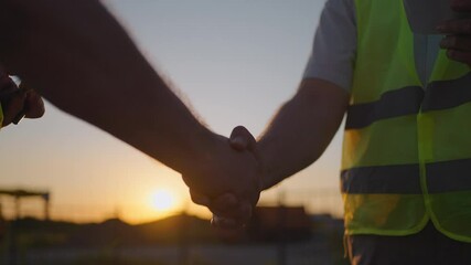 Portrait of hands of two builders. Builder shaking hand the builder on built house background. Close up of a handshake of two men in green signal vests against the background of the sun - Powered by Adobe