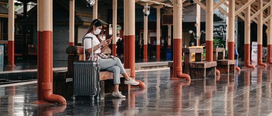 Naklejka na ściany i meble Asian tourist teenage girl at train station using smartphone for online map, social media check-in, or buy ticket booking. Modern travel app technology, lone traveler.