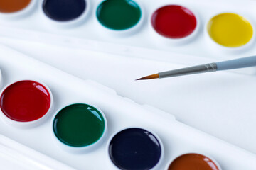 A set of watercolor paints and a paint brush on a white background with a copy of the space. Close-up