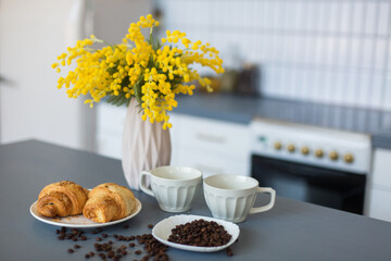 Coffee, croissants and yellow flowers in vase in the kitchen. Breakfast, home, coffee time concept