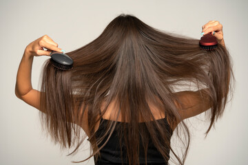 Rear view of a woman brushing her hair with two hair brushes