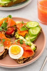 Healthy tasty breakfast, sandwiches with avocado and salmon, cucumbers and tomatoes, radishes and microgreens of peas with boiled egg, grapefruit smoothie in a glass