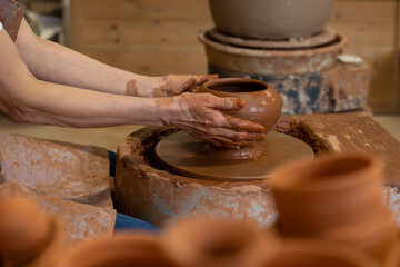 Sculptor in the studio makes a clay pot close-up. Senior woman is sculpting a bowl behind a rotating potter's wheel