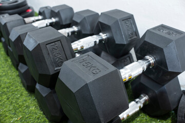 A row of hex dumbbells laid on an artificial grass mat. Workout equipment at a home gym.