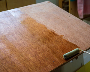 Applying polyurethane on the wooden board with roller. - obrazy, fototapety, plakaty