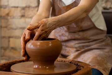Sculptor in the studio makes a clay pot close-up. Senior woman is sculpting a bowl behind a rotating potter's wheel