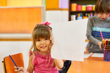 Child proudly shows drawing on sheet of paper in daycare