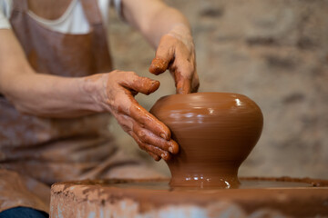 Sculptor in the studio makes a clay pot close-up. Senior woman is sculpting a bowl behind a rotating potter's wheel