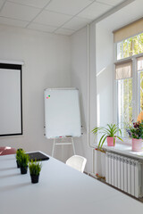Working place, table, windowsill with potflowers, whiteboard, projector on wall. Minimalists clean office, work space. Vertical shot.