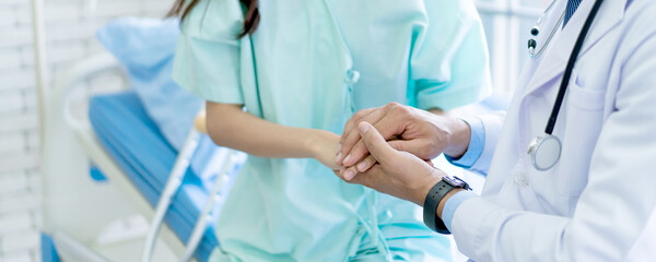 Caring caucasian doctor holding on Asian patient's hands in hospital to embolden unwell patient. 