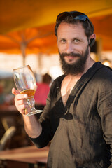 Bearded man posing for photographs, holding a glass of beer looks happy and satisfied in a pub. Portrait of an attractive bearded male with raised his glass of alcohol in his hand.Vertical orientation