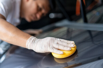 Cheerful Asian man cleaning and rubbing a car exterior by using sponge. 