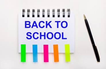 On a light background, a pen, a notebook with the text BACK TO SCHOOL and bright stickers.
