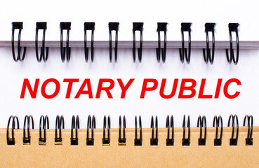 Text NOTARY PUBLIC on white paper between white and brown spiral notepads.