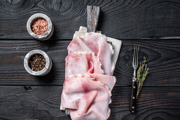 Sliced prosciutto ham on wooden board with herbs. Black wooden background. Top view