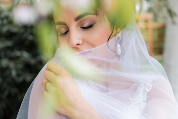 Portrait of young bride holding blurred veil outdoors