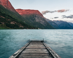 Stairs leading to a lake in the water surrounded by mountains and a red sunset