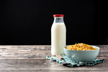 Corn flakes in a blue bowl and milk bottle on rustic wooden table. Copy space