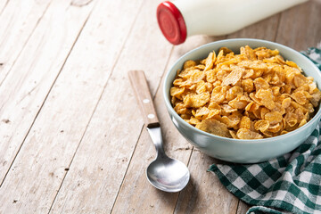 Corn flakes in a blue bowl and milk bottle on rustic wooden table. Copy space