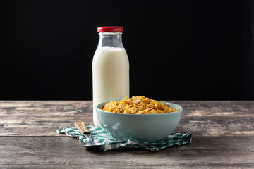 Corn flakes in a blue bowl and milk bottle on rustic wooden table