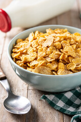 Corn flakes in a blue bowl and milk bottle on rustic wooden table