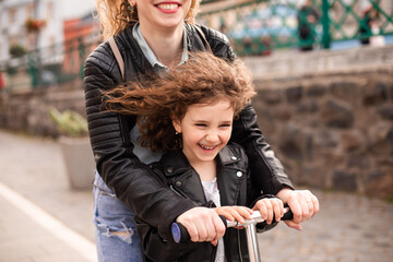 Obraz premium Mom and daughter ride a scooter and have a great time